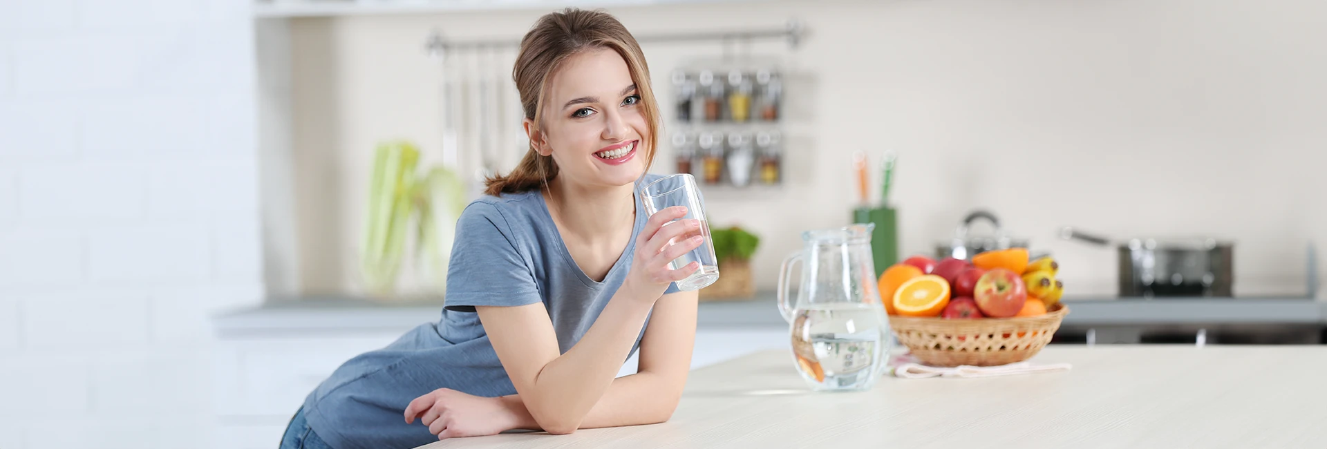 Une jeune femme souriante boit un verre d'eau dans sa cuisine