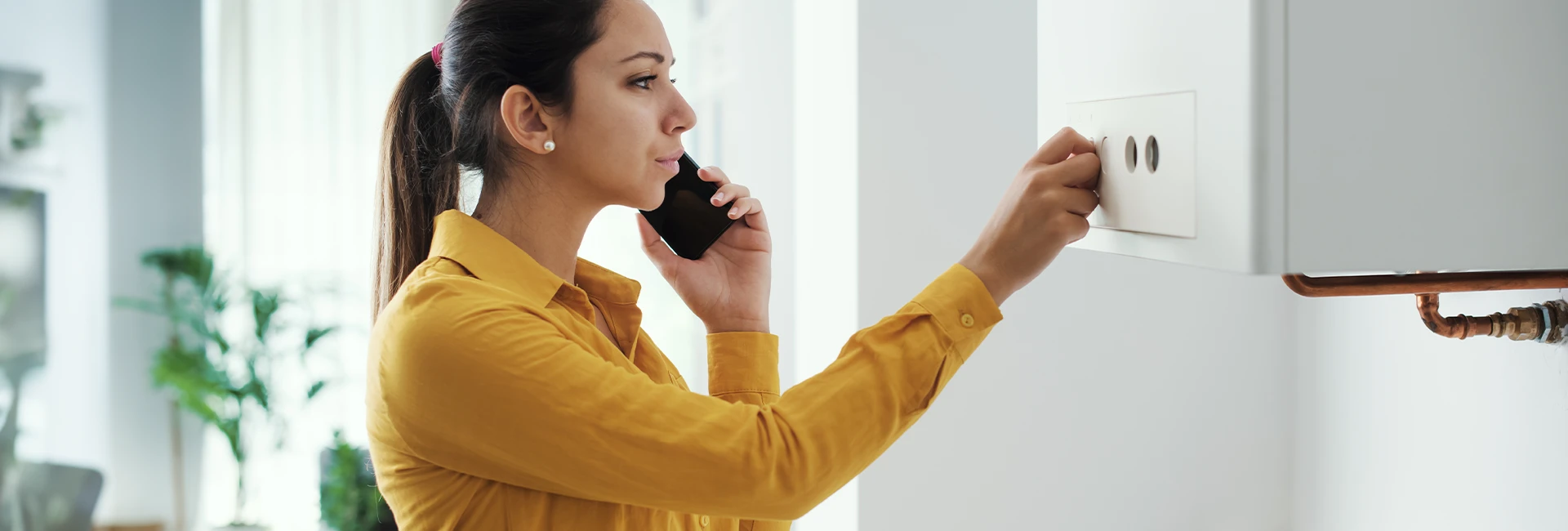 Une jeune femme au téléphone suit les consignes de son chauffagiste face à sa chaudière en panne